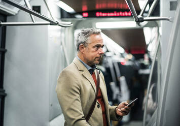 Reifer, gut aussehender Geschäftsmann mit Smartphone, der mit der U-Bahn in Prag unterwegs ist. - HPIF23164