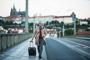 Mature handsome businessman with suitcase walking on a bridge in Prague city. Copy space. - HPIF23168