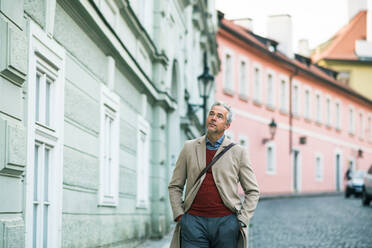Ein reifer Geschäftsmann, der auf einer Straße in Prag spazieren geht, die Hände in den Taschen, Kopierraum. - HPIF23182