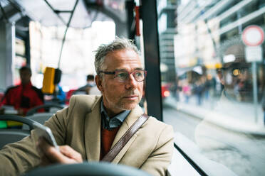 Reifer, gut aussehender Geschäftsmann mit Smartphone, der mit dem Bus in der Stadt Prag unterwegs ist. - HPIF23185