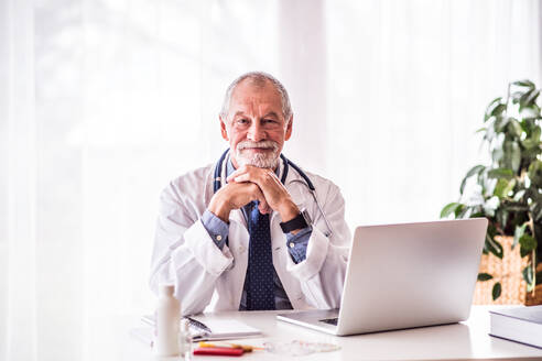 Älterer männlicher Arzt mit Laptop, der am Bürotisch sitzt. - HPIF23192