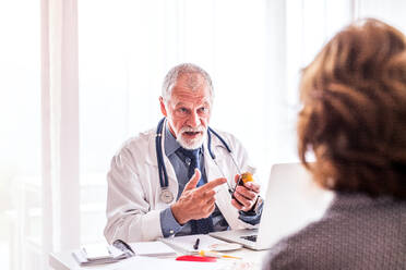 Male doctor with laptop talking to a senior woman in his office. - HPIF23195