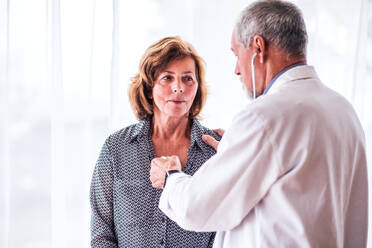 Male doctor examiming a senior woman with stethoscope in his office. - HPIF23200