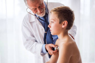 Senior male doctor examining a small boy with stethoscope in his office. - HPIF23208