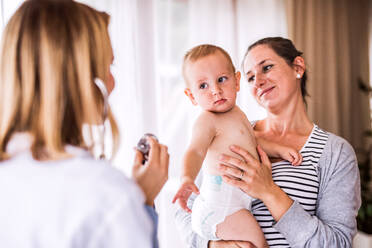 Junge Ärztin, die ein Baby in ihrer Praxis untersucht. Junge Mutter hält einen Jungen. - HPIF23223