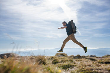 Seitenansicht eines reifen Mannes mit Rucksack beim Wandern in den Bergen im Sommer, beim Springen. - HPIF23242