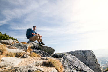 Mature man with backpack hiking in mountains in autumn, resting on rock. - HPIF23248