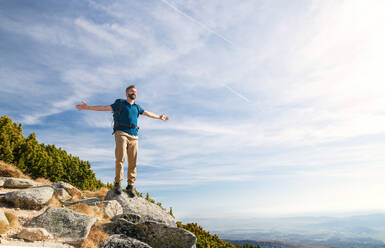 Mature man with backpack hiking in mountains in summer, resting with arms stretched. - HPIF23249