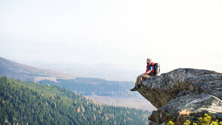 Älterer Mann mit Rucksack, der im Herbst in den Bergen wandert und sich auf einem Felsen ausruht. Kopierraum. - HPIF23262