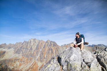 Älterer Mann mit Rucksack, der im Herbst in den Bergen wandert und sich auf einem Felsen ausruht. Kopierraum. - HPIF23270