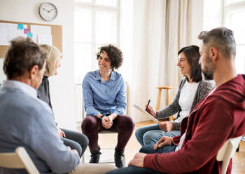 Ernste Männer und Frauen, die während einer Gruppentherapie im Kreis sitzen und sich unterhalten. - HPIF23291