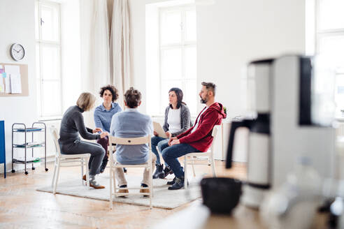 Ernste Männer und Frauen, die während einer Gruppentherapie im Kreis sitzen und sich unterhalten. - HPIF23292