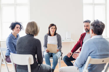 Ernste Männer und Frauen, die während einer Gruppentherapie im Kreis sitzen und sich unterhalten. - HPIF23293