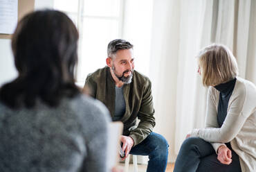 Älterer Mann und ältere Frauen sitzen während einer Gruppentherapie im Kreis und unterhalten sich. - HPIF23300