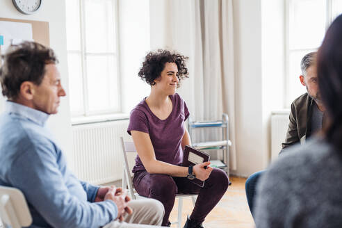 Ernste Männer und Frauen, die während einer Gruppentherapie im Kreis sitzen und sich unterhalten. - HPIF23301