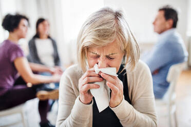 Ein Porträt einer älteren depressiven Frau, die während einer Gruppentherapie weint und sich die Nase putzt. - HPIF23318