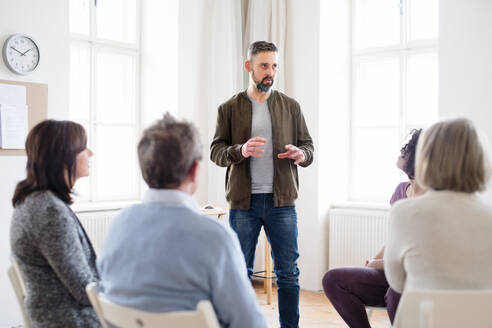 Ein reifer Mann, der während einer Gruppentherapie mit anderen Menschen spricht. - HPIF23324