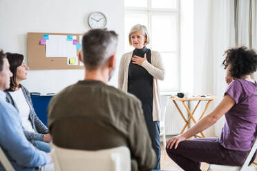 A senior woman standing and talking to other people during group therapy. - HPIF23326