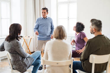 Ein reifer Mann, der während einer Gruppentherapie mit anderen Menschen spricht. - HPIF23327