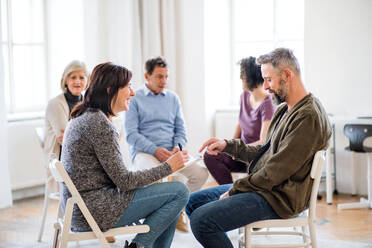 A senior counsellor with clipboard talking to a man during group therapy. - HPIF23329