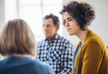 Ernste Männer und Frauen, die während einer Gruppentherapie im Kreis sitzen und sich unterhalten. - HPIF23338