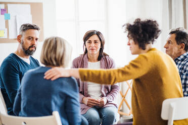 Serious men and women sitting in a circle during group therapy, supporting each other. - HPIF23339