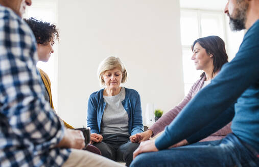 Männer und Frauen, die während einer Gruppentherapie im Kreis sitzen und sich an den Händen halten, mit geschlossenen Augen. - HPIF23349