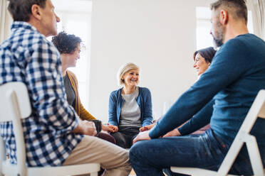 Männer und Frauen, die während einer Gruppentherapie im Kreis sitzen, sich an den Händen halten und lachen. - HPIF23350