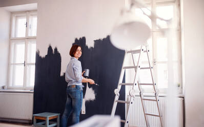 A portrait of young creative woman painting wall black. A startup of small business. - HPIF23369