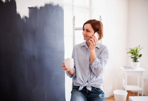 Ein Porträt der jungen kreativen Frau mit einer Tasse Kaffee und Smartphone Malerei Wand schwarz. - HPIF23378