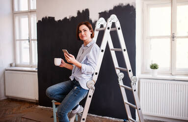Ein Porträt der jungen kreativen Frau mit einer Tasse Kaffee und Smartphone Malerei Wand schwarz. - HPIF23379
