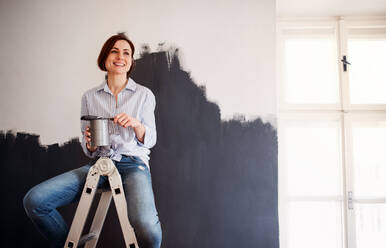 Ein Porträt einer jungen kreativen Frau, die eine Wand schwarz anmalt, ein Start-up für ein kleines Unternehmen. - HPIF23386