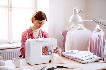 Young creative woman in a studio, working on sewing machine. A startup of small tailoring business. - HPIF23427