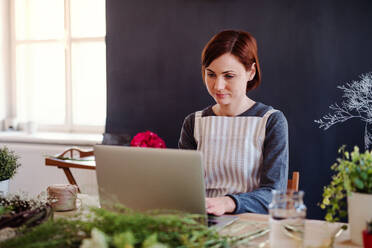 Eine junge kreative Frau arrangiert Blumen in einem Blumenladen mit einem Laptop. - HPIF23434