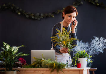 Eine junge, kreative Frau arrangiert mit ihrem Smartphone Blumen in einem Blumenladen, einem Startup-Unternehmen für Blumen. - HPIF23441
