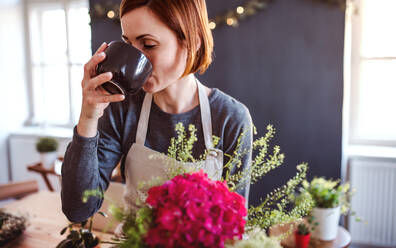 Eine junge, kreative Frau mit einem Kaffee, die in einem Blumenladen Blumen arrangiert, eine Neugründung eines Blumenladens. - HPIF23460