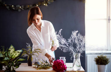 Eine junge, kreative Frau, die in einem Blumenladen Blumen arrangiert, eine Neugründung eines Blumenladens. - HPIF23466