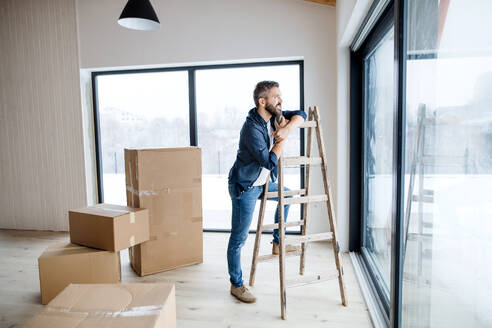 Ein reifer Mann mit Pappkartons, der am Fenster steht und ein neues Haus einrichtet. Ein neues Hauskonzept. Raum kopieren. - HPIF23516