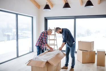 Ein fröhlicher älterer Mann, der seinem reifen Sohn bei der Einrichtung eines neuen Hauses hilft, ein neues Wohnkonzept. - HPIF23521