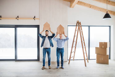 Zwei Männer, die kleine Holzhäuser auf dem Kopf tragen, wenn sie ein neues Haus einrichten, ein neues Wohnkonzept. - HPIF23539