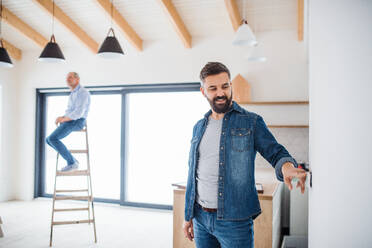 Ein fröhlicher älterer Mann, der seinem reifen Sohn bei der Einrichtung eines neuen Hauses hilft, ein neues Wohnkonzept. - HPIF23554