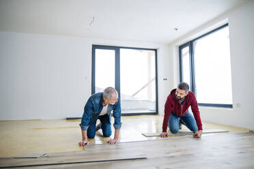 A front view of mature man with his senior father laying wood flooring, a new home concept. - HPIF23557