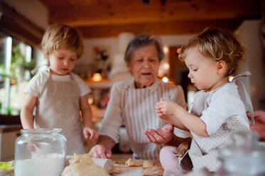 Glückliche ältere Urgroßmutter mit kleinen Kleinkindern, die zu Hause Kuchen backen. - HPIF23568