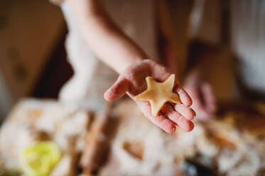 Ein Mittelteil eines kleinen Jungen, der zu Hause Kuchen backt, eine Nahaufnahme einer Hand, die einen Keks hält. - HPIF23574