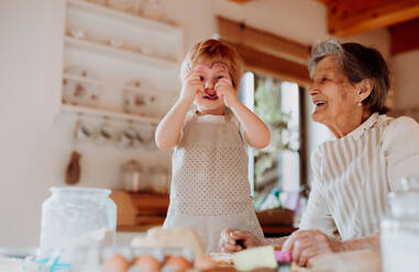 Glückliche ältere Urgroßmutter mit einem kleinen Jungen im Kleinkindalter, der zu Hause Kuchen backt. - HPIF23585