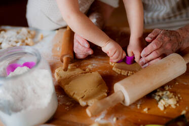 Ein Mittelteil einer älteren Urgroßmutter mit einem kleinen Kleinkind, das zu Hause Kuchen backt. - HPIF23591