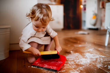 A small toddler girl with brush and dustpan sweeping messy floor in the kitchen at home. - HPIF23597