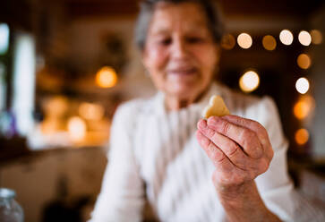 Nahaufnahme einer glücklichen älteren Frau, die zu Hause in einer Küche Kuchen backt und einen Keks hält. - HPIF23601