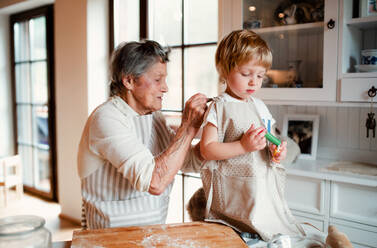 Glückliche ältere Urgroßmutter mit einem kleinen Jungen im Kleinkindalter, der zu Hause Kuchen backt. - HPIF23607