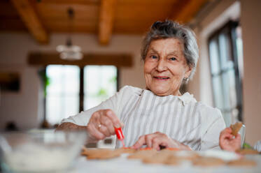 Eine ältere Frau, die zu Hause in einer Küche Kuchen backt und verziert. Kopierraum. - HPIF23611